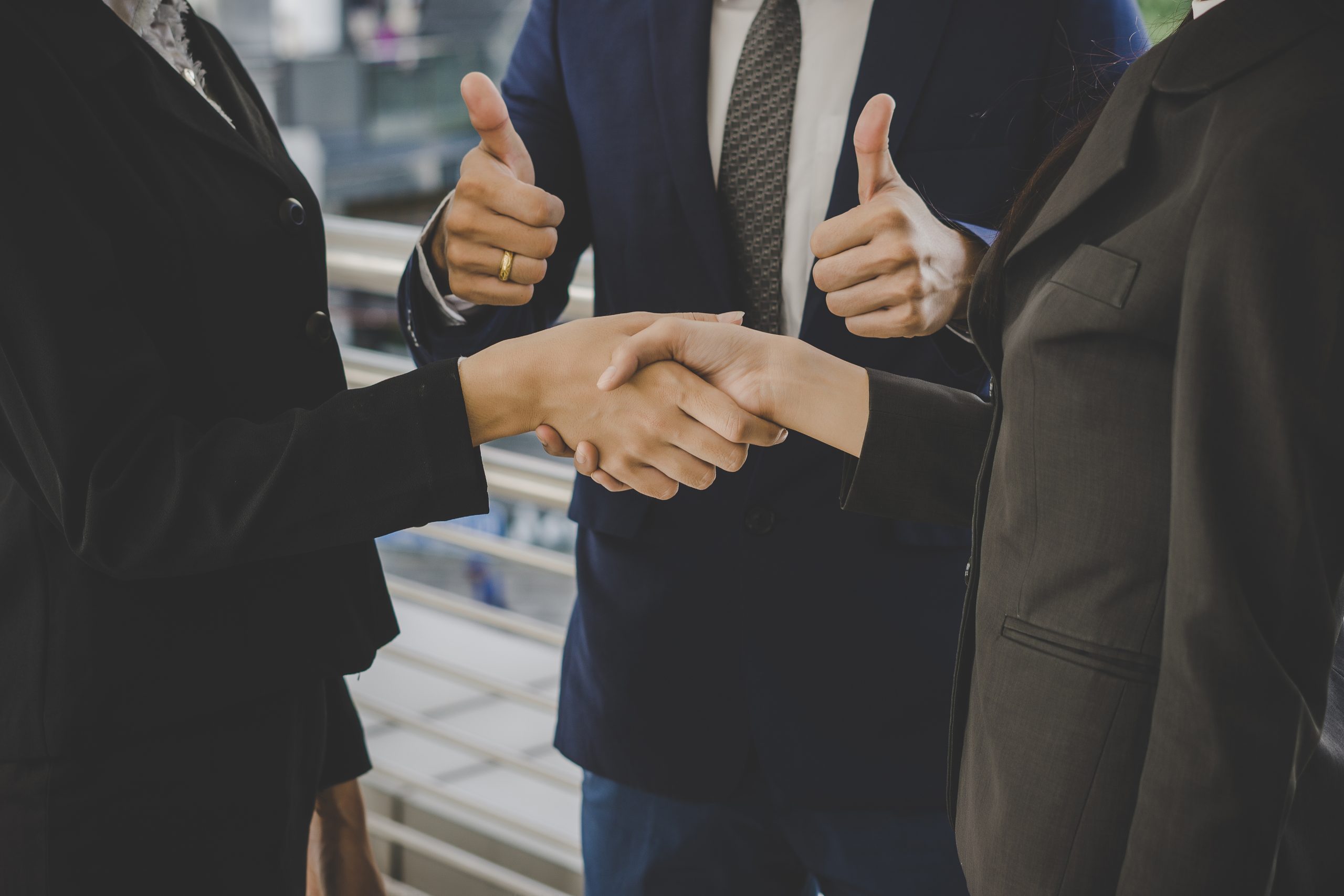 Business professionals shaking hands with colleagues giving thumbs up after sealing a deal