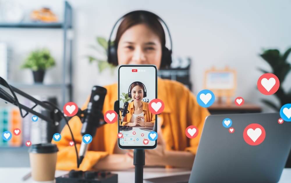 Young woman in headphones livestreaming on a smartphone with heart and like reactions floating up