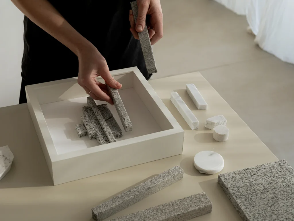 Designer arranging stone and marble material samples in a minimalist tray for a brand palette