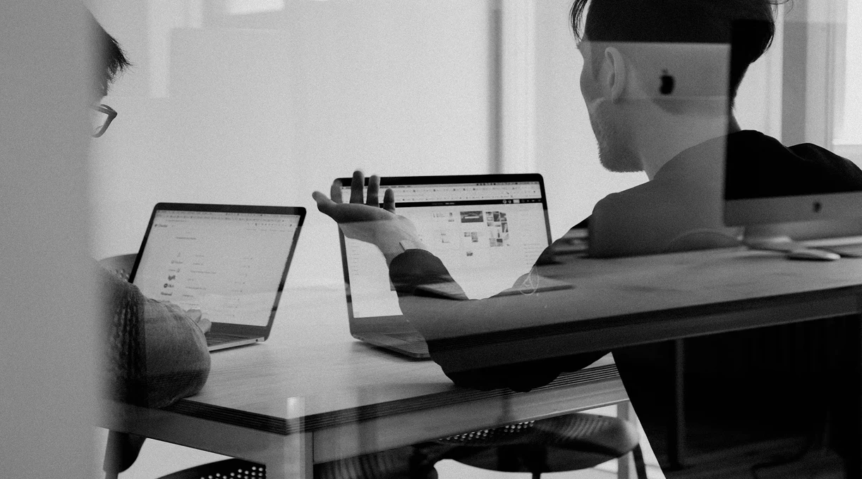 Two colleagues reviewing analytics on laptops across a desk in a strategy meeting